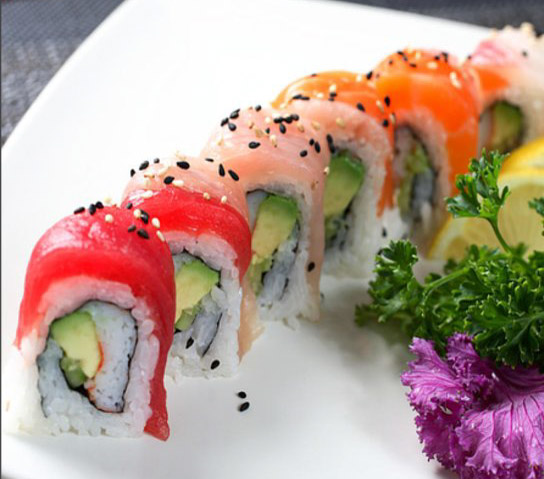 This is a picture of a rainbow roll put in a line with lemons and lettuce on the side.